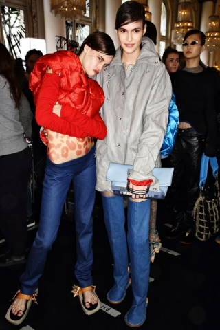 Zwei Models tragen im Backstage-Bereich bei Acne Studios eine rote und eine graue Daunenjacke. Dazu kombinieren sie Jeans.