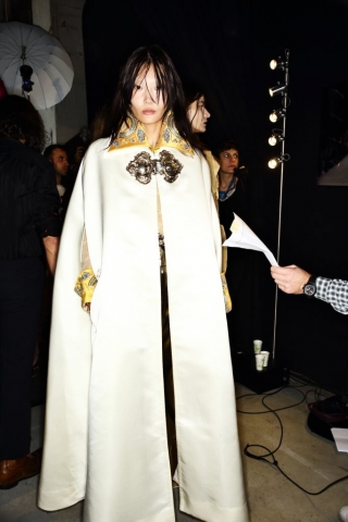 Das Model trägt auf diesem Bild ein bodenlanges, weißes Cape mit großer Zierschnalle von Designerin Vivienne Westwood.