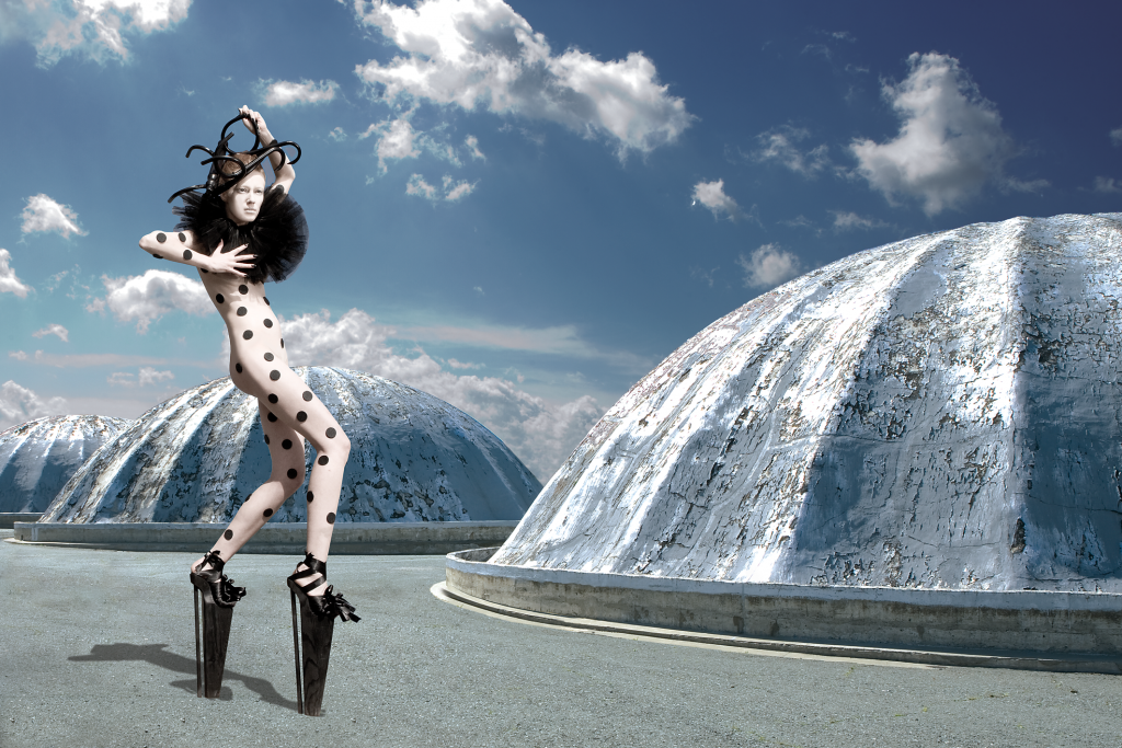 Auf dem Bild ist ein Model einer futuristisch anmutebden Gebirgslandschaft zu sehen Sie trägt einen weißen Catsuit mit schwarzen Punkten.