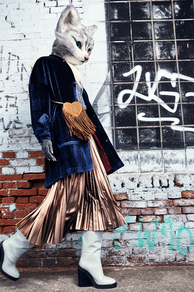 Fashion-Mieze Pheline von Fou de Pheline kombiniert ein oversized Samt-Sakko von Stine Goya zu einem kupferfarbenem, glänzendem Plissee-Rock von Tara Jarmon. Helle Stiefel von Hermès, eine braune Fransen-Tasche in Herzform von Saint Laurent und ein Karohemd komplettieren den Look.