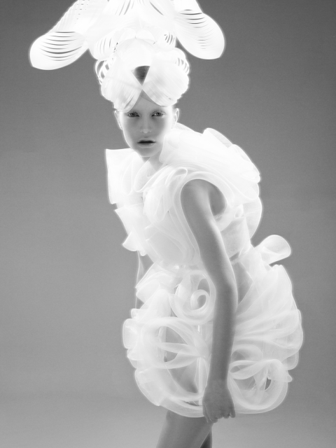 Auf der Modefotogarfie ist einen Model einem weißen, sklupturalen Kleid zu sehen. Auf dem Kopf trägt das Mädchen einen ausladenden, weißen Hut. Designer: Tanel Veenre. Foto: Woland. Buch: Otherworldly. © Gestalten 2016