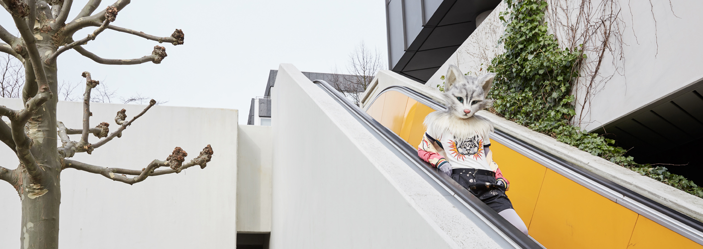 Auf den Fotos ist Katzenlady Pheline an und auf einer gelben Rolltreppe zu sehen. Sie trägt einen Blouson von Tsumori Chisato, eine schwarze shiny Shorts von Dries van Noten, ein T-Shirt von Gucci und gelbe Sneakers von Hermès.