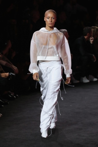 Auf dem Foto ist das Model Adwoa Aboah zu sehen. Sie befindet sich auf der Fashion Show von FENTY Puma by Rihanna. Sie trägt einen trasparenten weißen Hoodie, eine weiße Jogginghose mit seitlicher Schnürung und spitze, weiße Booties.