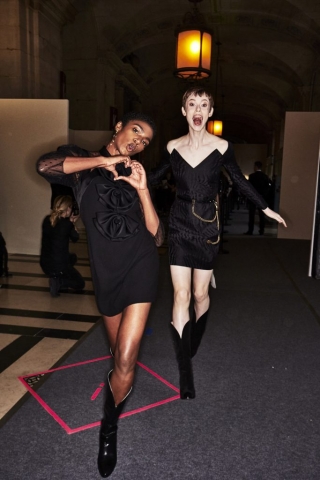 Auf dem Foto sind zwei Models im Backstage-Bereich der ersten Modenschau von Designerin Claire Waight Keller für das Modehaus Givenchy in Paris zu sehen. Es handelt sich um die Präsentation der F/S 2018 Kollektion. Beide Models tragen schwarze kurze Kleider. Dazu kombinieren sie Cowboystiefel.