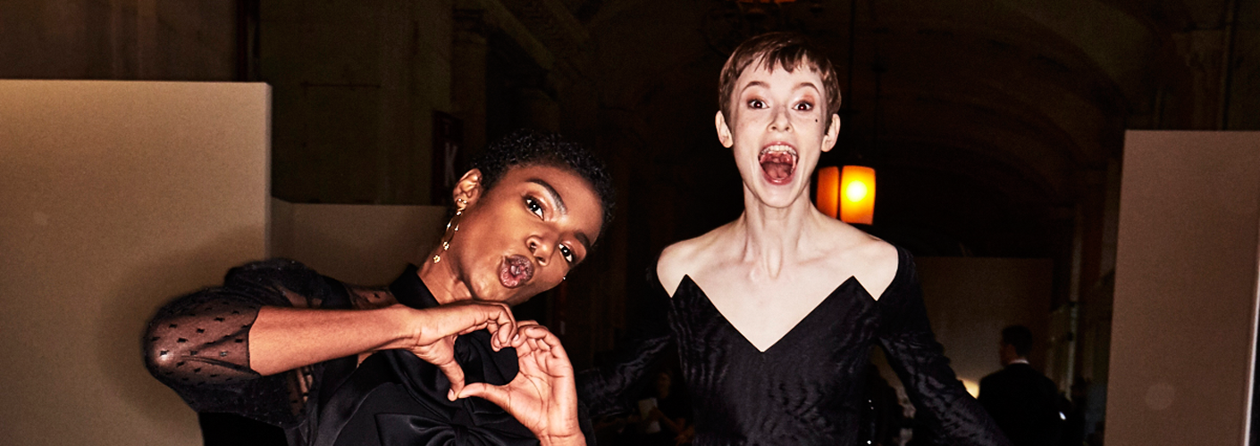 Auf dem Foto sind zwei Models im Backstage-Bereich der ersten Modenschau von Designerin Claire Weight für das Modehaus Givenchy in Paris zu sehen. Es handelt sich um die F/S 2018 Kollektion. Beide Models tragen schwarze kurze Kleider.