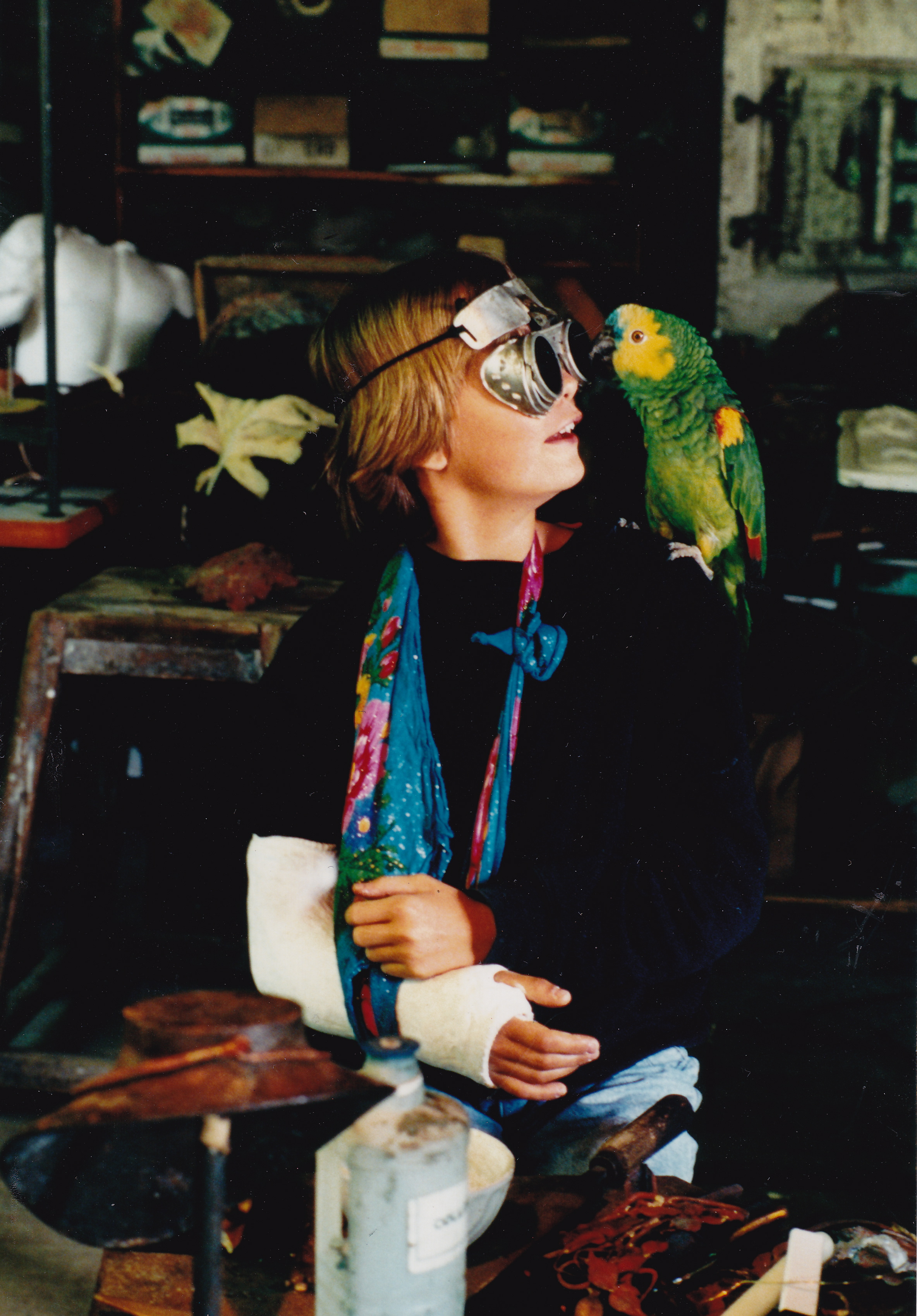Auf dem Foto ist die Künstlerin Clémentine de Chabaneix als junges Mädchen zu sehen. Sie trägt den rechten Arm in Gips. Auf iherer linken Schulter sitzt ein grüner Papagei namens Willy.