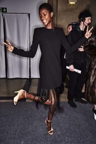 Im Backstage-Bereich der Givenchy Herbst/Winter 2018 Show trägt ein Model ein schwarzes Kleid mit langen, feinen Fransen am Saum.
