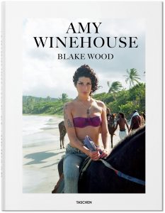 Auf dem Foto ist das Cover des Bildbands "Amy Winehouse by Blake Wood", erschienen im Taschen Verlag zu sehen. Am sitzt auf einem Pferd, tragt ein pinkes Bikini-Oberteil und eine Jeans und reitet barfuß am Plantation Beach in Saint Lucia. Das Foto stammt aus dem Jahr 2009.